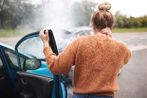 A woman getting out of a car and holding the back of her neck after an auto accident, soon needing to call an Injury Attorney in Peoria IL